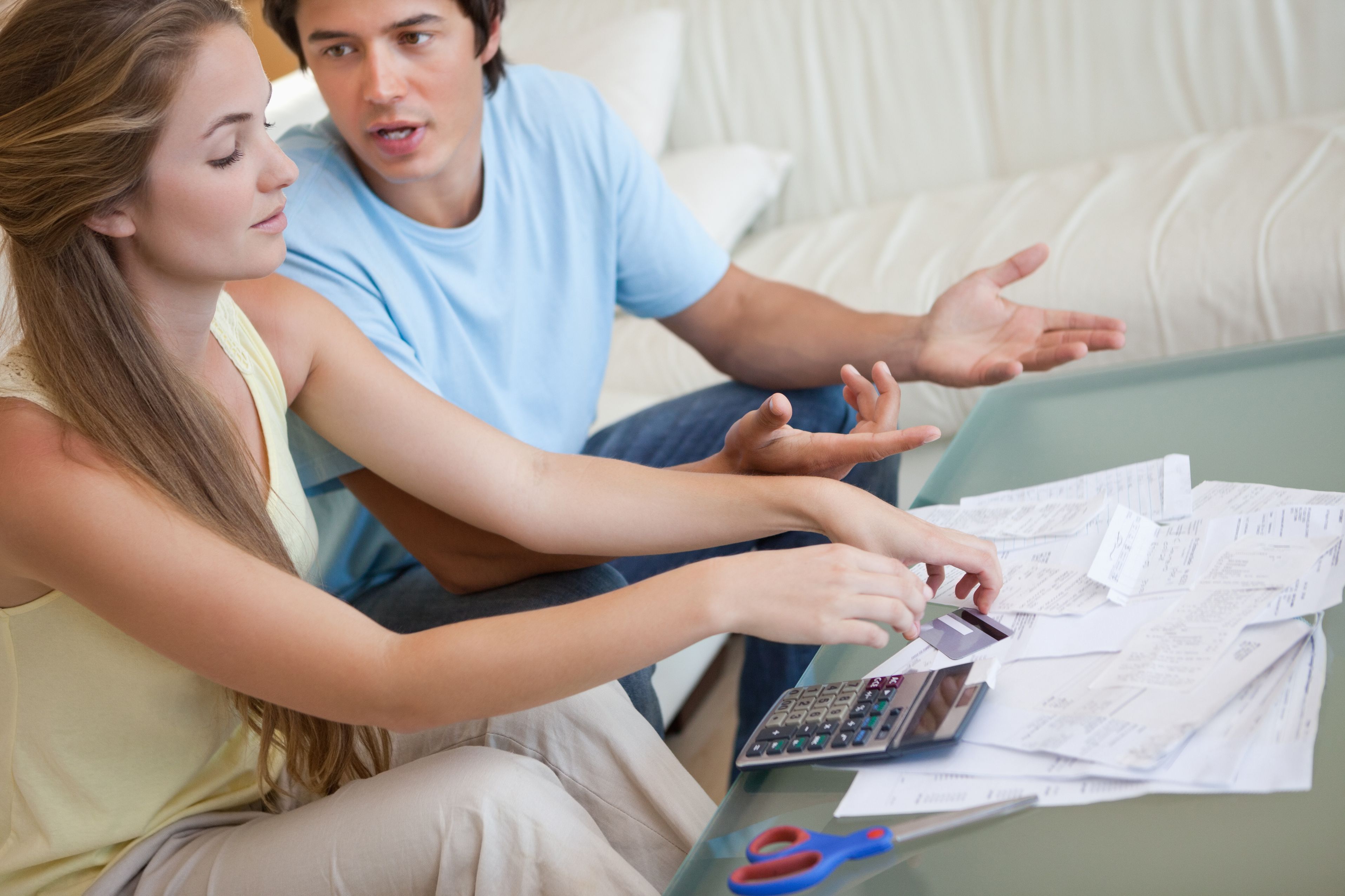  A couple is sitting on a couch in their living room looking at bills and receipts with a calculator on the table.